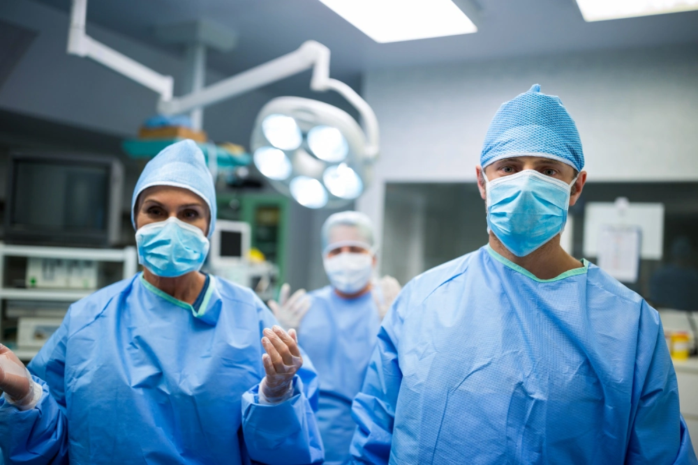 A team of surgeons and medical staff in blue scrubs and masks prepared for a procedure in a modern operating room.